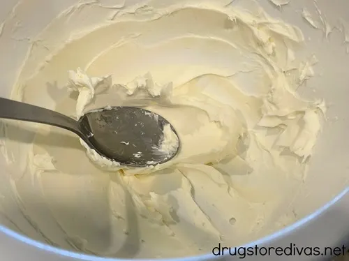 Cream cheese and a silver spoon in a white bowl.