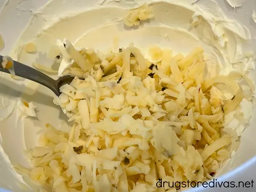 Grated pepper jack cheese in a bowl with a silver spoon and cream cheese.