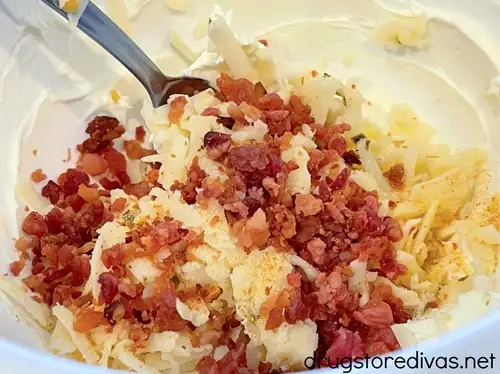 Bacon bits, grated pepper jack cheese in a bowl with a silver spoon and cream cheese.