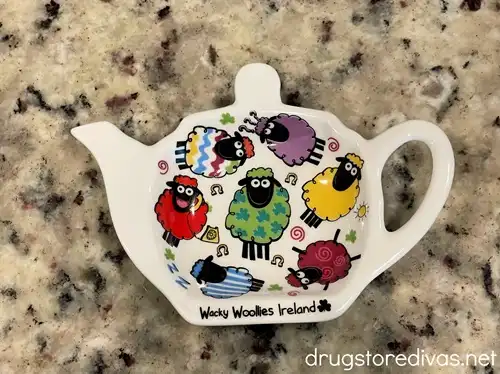 A tea kettle-shaped tea bag holder with colorful sheep on it.