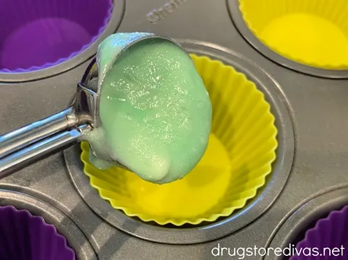 Green batter being added to a yellow cupcake holder via a cookie scoop.