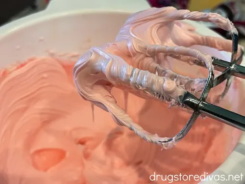 Pink icing in a white bowl with two hand mixer beaters with pink icing above it.