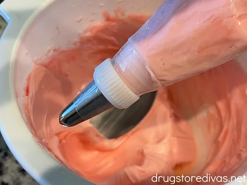 Pink icing in a piping bag with a silver tip above a white bowl filled with pink icing.