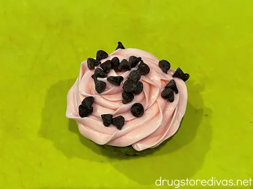 Mini chocolate chips on top of pink icing on a green cutting board.