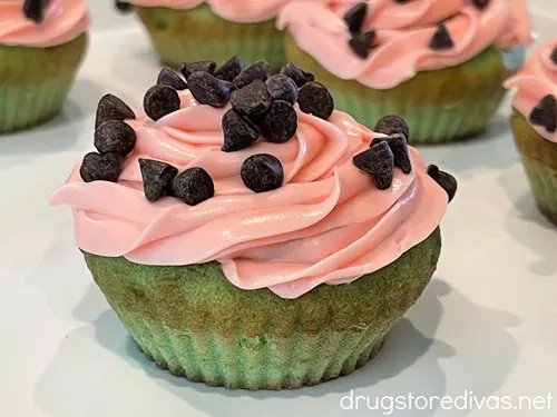 A white tray filled with green cupcakes with pink icing and mini chocolate chips on top that are meant to look like watermelon.