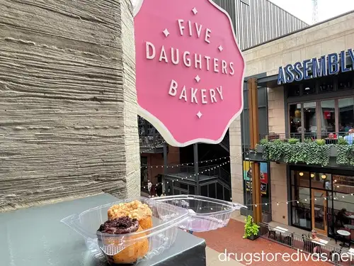 Two doughnuts in a plastic container in front of a pink sign that says Five Daughters Bakery at Assembly Food Hall in Nashville.