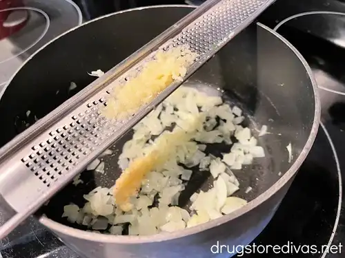 Grated garlic on a microplane over a saucepan with chopped garlic in it.