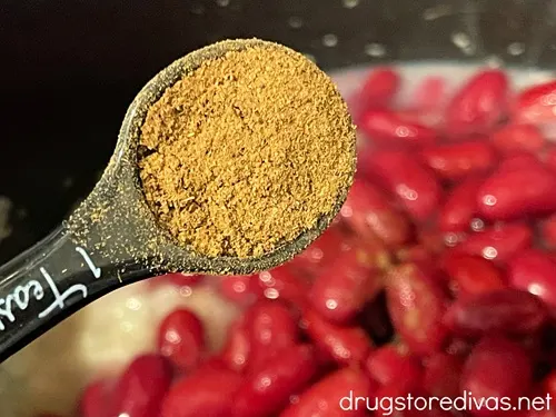 Seasoning in a measuring spoon above red kidney beans in a saucepan.