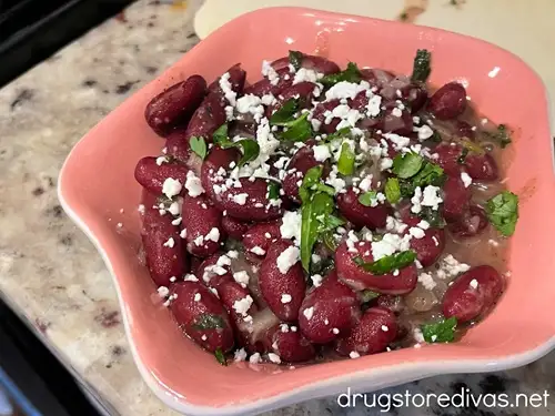 Dark red kidney beans, topped with cotija cheese and cilantro, in a pink bowl.