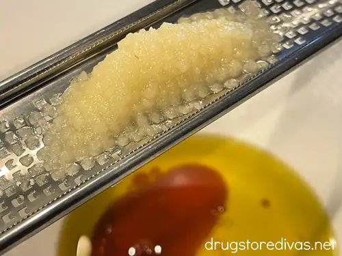 Garlic on a microplane zester above a white bowl with olive oil in it.