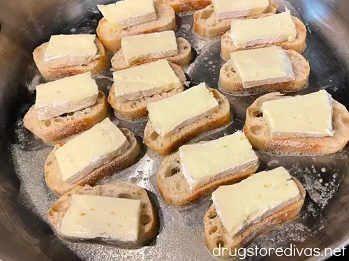 Pieces of French bread with brie slices on them in a silver skillet.