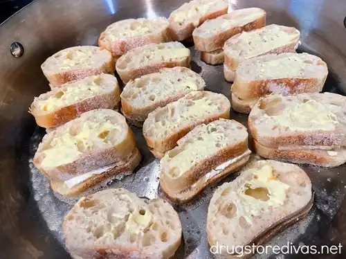 Pieces of French bread with butter on top in a silver skillet.