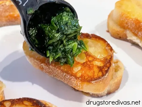 A spoonful of chimichurri being put on top of a mini grilled cheese sandwich.