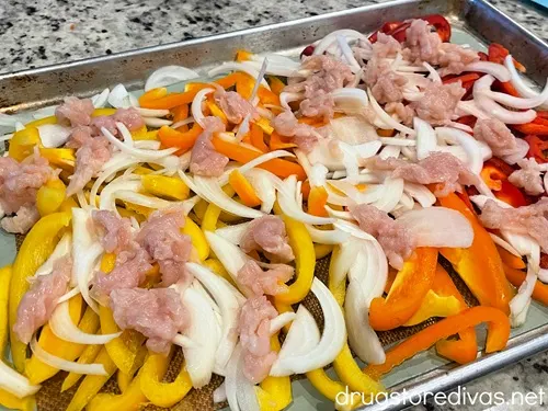 Pieces of raw chicken on top of sliced onion and yellow, orange, and red peppers.