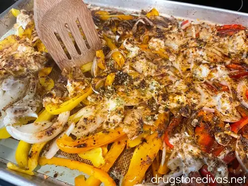 Sheet pan chicken fajitas ingredients being stirred with a bamboo spoon.