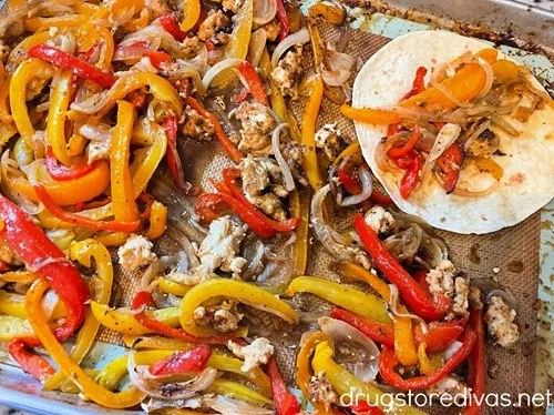 Cooked sheet pan chicken fajitas ingredients on a sheet pan with a filled tortilla on the side.