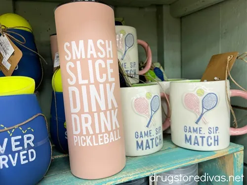 A pink tumbler that's on a shelf with mugs around it.