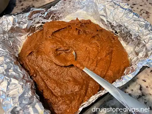 Pumpkin brownie batter in a foil lined pan with a spoon on top.
