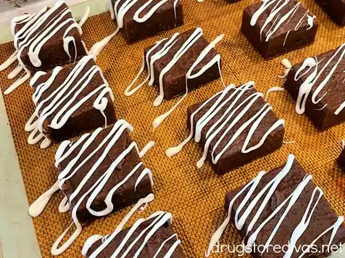 Cut brownies with white chocolate lined drizzled on them on a baking sheet.