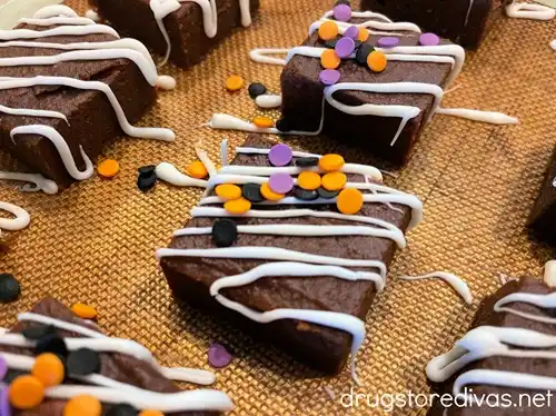 Brownies decorated with white lines and black, orange, and purple circle sprinkles, with those same sprinkles around them, on a baking mat.