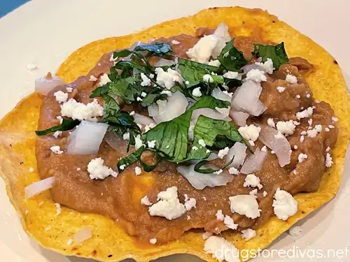 Cotija cheese crumbles, chopped cilantro and onions, and refried beans on a tostada shell.