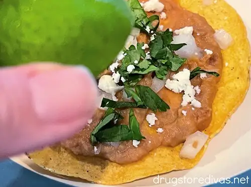 A hand squeezing lime on top of a bean tostada on a plate.
