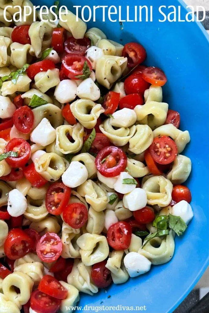 Tortellini, sliced tomato, mozzarella pieces, and basil in a blue bowl with the words "Caprese Tortellini Salad" digitally written on top.