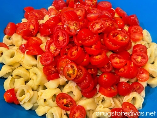 Sliced cherry tomatoes on top of cooked tortellini in a blue bowl.