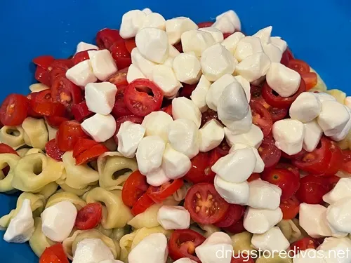 Mozzarella pearls and sliced cherry tomatoes on top of cooked tortellini in a blue bowl.