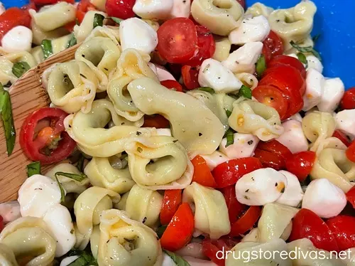 Caprese tortellini salad in a blue bowl being mixed by a bamboo spoon.