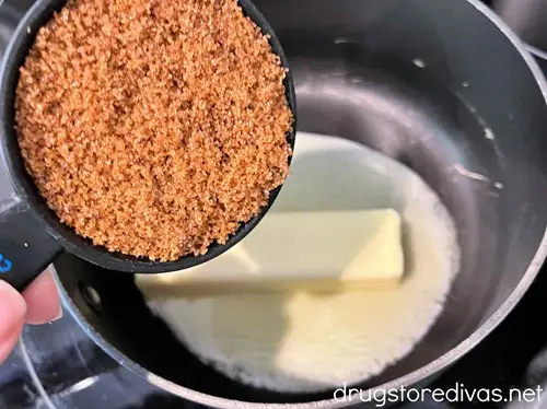 Brown sugar in a measuring cup above a stick of butter that's starting to melt in a stock pot.