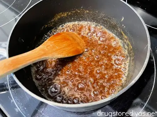 A caramel-colored mixture that's bubbling in a sauce pan that also has a bamboo spoon in it.
