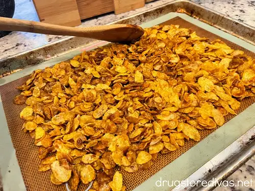 Corn flakes on a silicone baking mat-lined cookie sheet with a bamboo spoon shaping them.