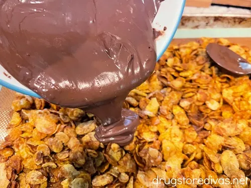 Melted chocolate in a bowl being poured on top of corn flakes.