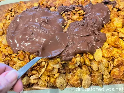 A spoon smoothing chocolate on top of corn flakes.