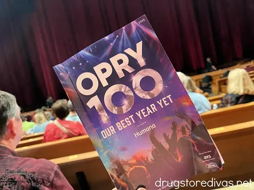 A playbill for Opry 100 being held up in front of the Grand Ole Opry stage.