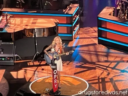 A blonde woman with a guitar on stage at the Grand Ole Opry.