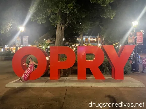 A woman sitting inside the O of a large sign that says OPRY at the Grand Ole Opry.