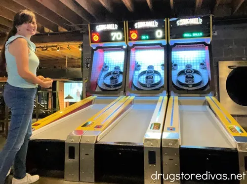 A woman in a blue tank top and jeans standing in front of three pinball machines at Pins Mechanical Co in Nashville.