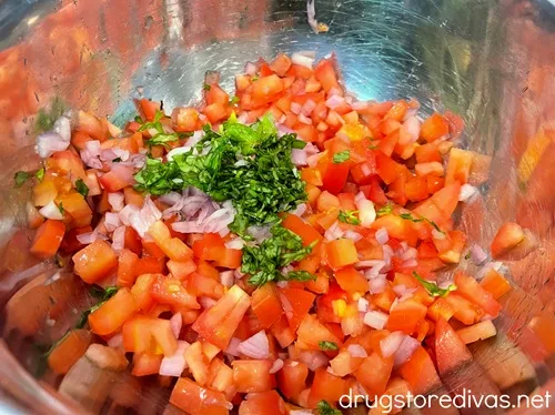 Diced tomatoes, shallots, and chopped basil in a silver bowl.