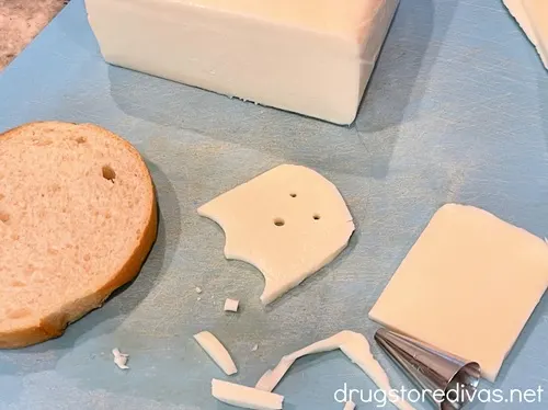 A ghost cut out of mozzarella cheese with a cheese block and scraps, and a piece of French bread, around it.