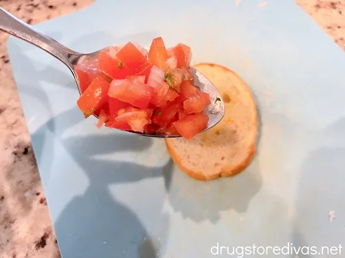 A spoon filled with bruschetta above a piece of bread.
