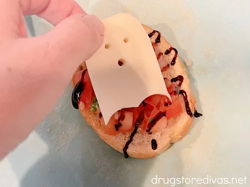 Fingers placing a mozzarella cheese ghost on top of a piece of bruschetta toast.