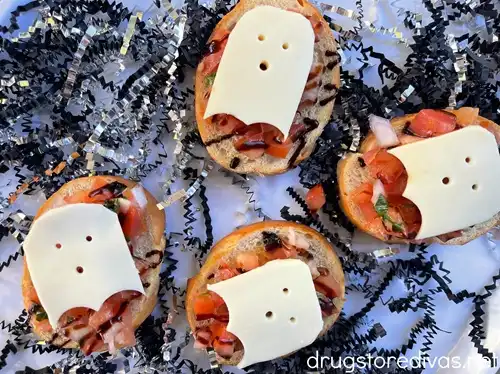 Four pieces of bruschetta with mozzarella cheese ghosts on top with black and silver paper shred around them.