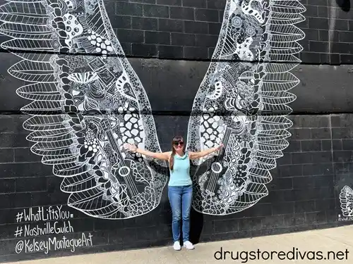 A woman in a blue tank top and jeans posing in front of the What Lifts You Up wings mural in Nashville.