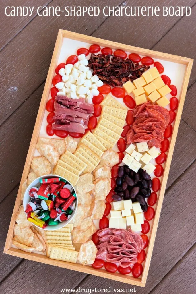 Meat, cheese, crackers, and chocolate arranged on a board in the shape of a candy cane with the words "Candy Cane Charcuterie Board" digitally written on top.