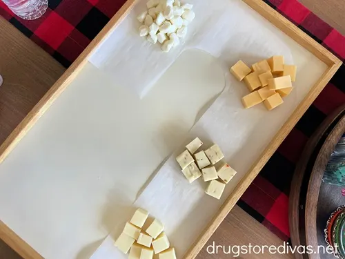 Four piles on cheese on top of a candy cane-shaped piece of parchment paper on a square charcuterie board.