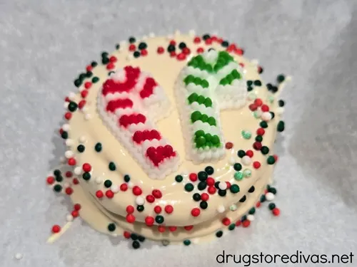 A white chocolate Oreo cookie with a green and red candy cane in the middle and green and red nonpareil sprinkles around the egde.