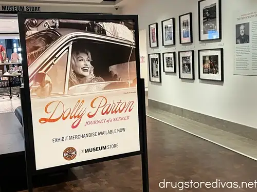 A sign advertising Dolly Parton merch next to a wall filled with photos at the Country Music Hall of Fame in Nashville.