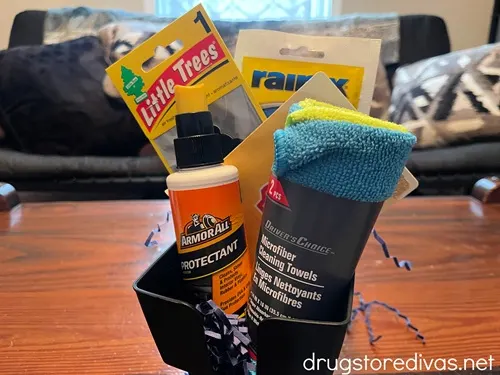 An air freshener, Rain X, ArmorAll, and a microfiber towel, plus, blue paper shred, in a car cup organizer.